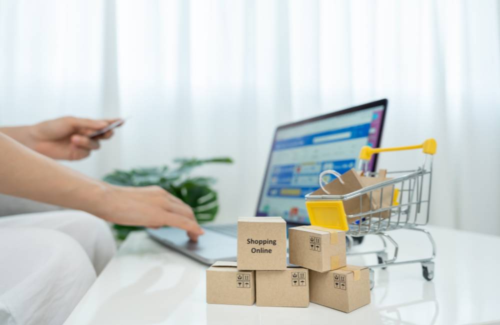 ノートパソコンの前に置かれた「Shopping Online」と書かれた段ボール箱と小さなショッピングカート