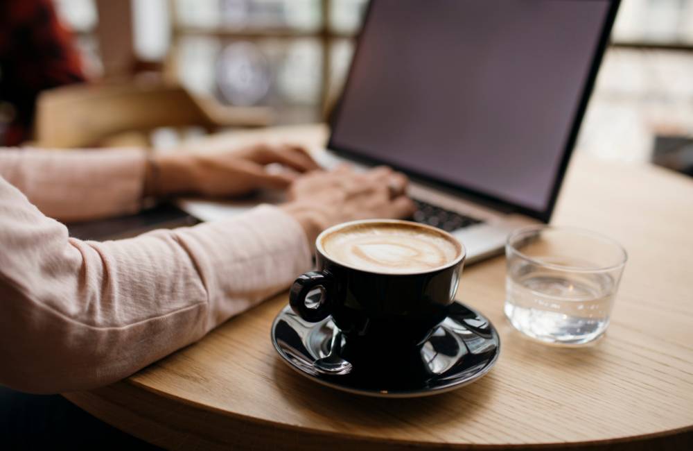 カフェのテーブルでコーヒーを傍らに置き、ノートパソコンで作業をするリラックスしたビジネスシーン