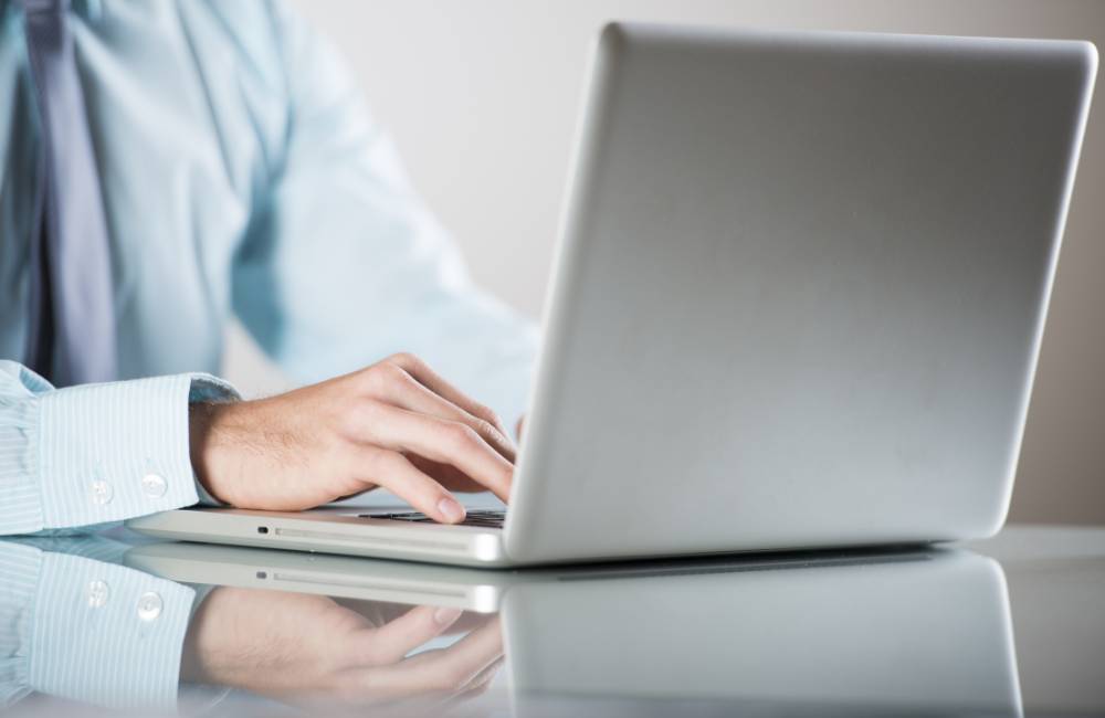 シャツを着たビジネスマンがスタイリッシュなノートパソコンを操作している様子。国内生産の信頼性と、ビジネスから個人利用まで幅広く支持されるマウスコンピューターのブランドイメージを表現しています.