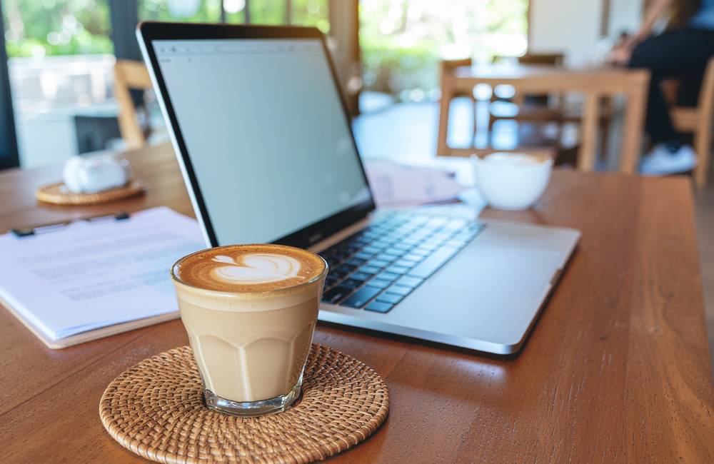 カフェのような落ち着いた雰囲気の木製テーブルに置かれたノートパソコンとコーヒー。自分に合った中古PCを手に入れ、充実したデジタルライフを送る様子を表現しています.