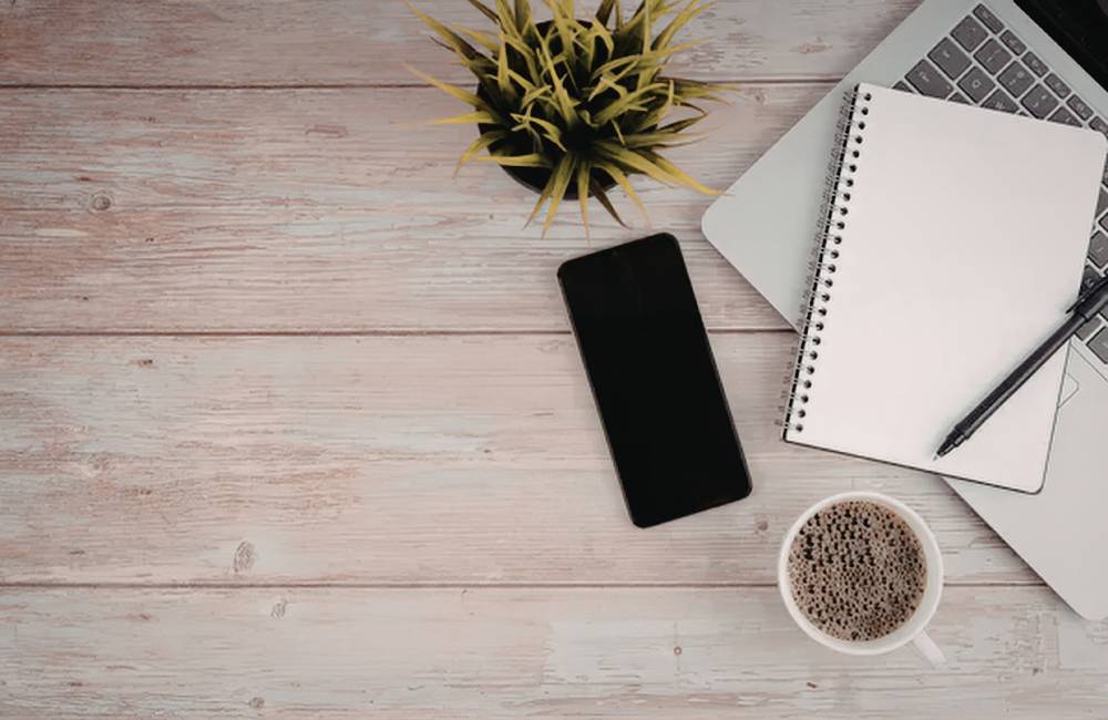 明るい窓辺の木製デスク。開いたノートパソコン（10.jpgと同じWPテーマ画面）、iPhone、そして付箋が置かれている。HPのノートパソコンと共に、充実したワークスペースと落ち着いた時間が共有されている様子。