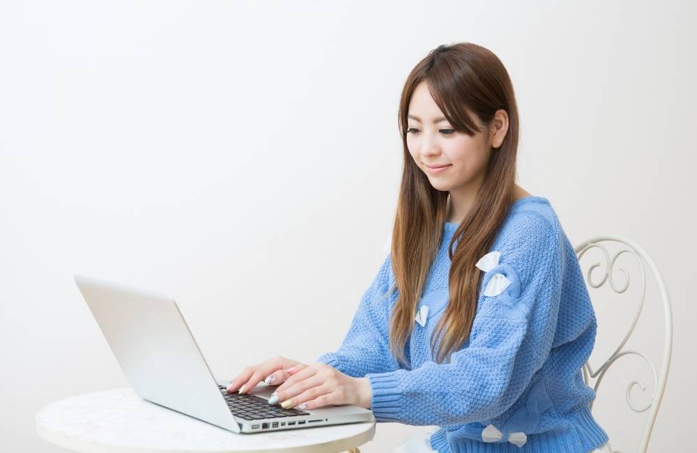 明るい部屋でノートパソコンを操作しながら、穏やかに微笑んでいる女性