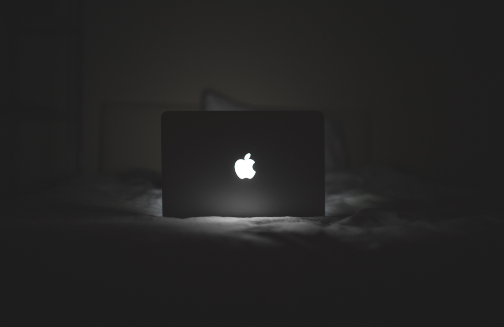暗闇の中でリンゴのマークだけが白く光っている、閉じた状態の古いMacBook