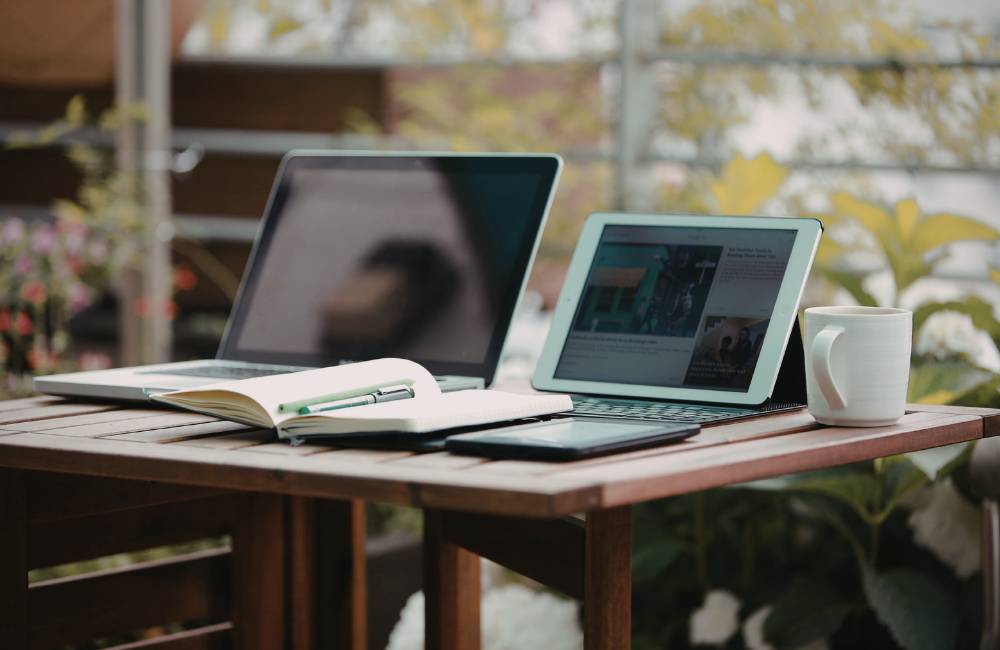 屋外のテラス席でノートPCやタブレット、ノートを広げて軽快に作業をする様子