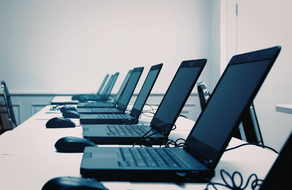 きれいに整頓された店舗や実習室のデスクの上に、一列に並んで陳列されている黒いノートパソコン