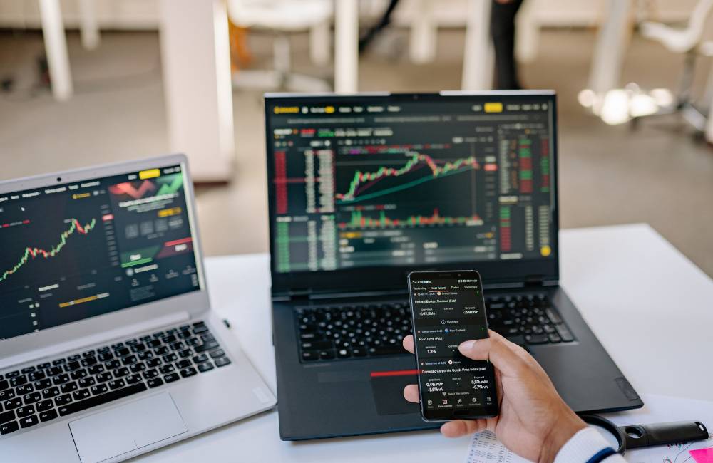 ノートパソコンの画面に複雑なデータチャートが表示されており、スマートフォンで数値を確認しながら性能をチェックしている様子