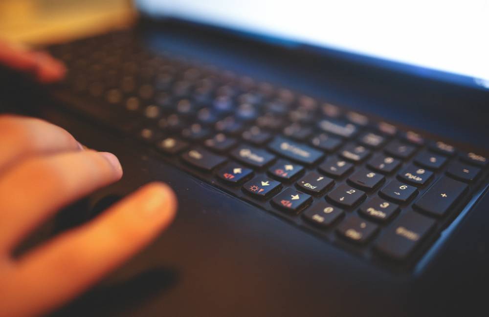 明るい場所でスマホを手にしながらパソコンを操作する女性。セール情報をチェックし、お得に買い物をするワクワク感を表現。