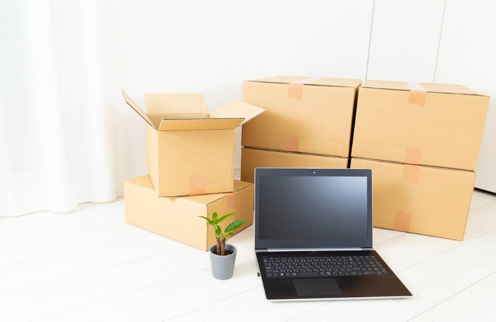 部屋に置かれた複数の段ボール箱とノートパソコン、観葉植物