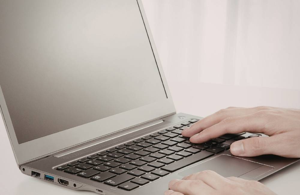 ノートパソコンのキーボードに手を添え、画面を見つめながら操作しているユーザーの手元のアップ。