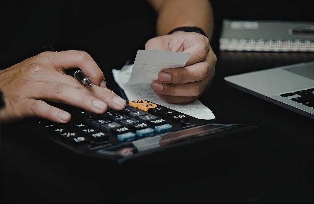 黒いデスクで、電卓を叩きながら手に持った領収書を確認している手元のアップ。