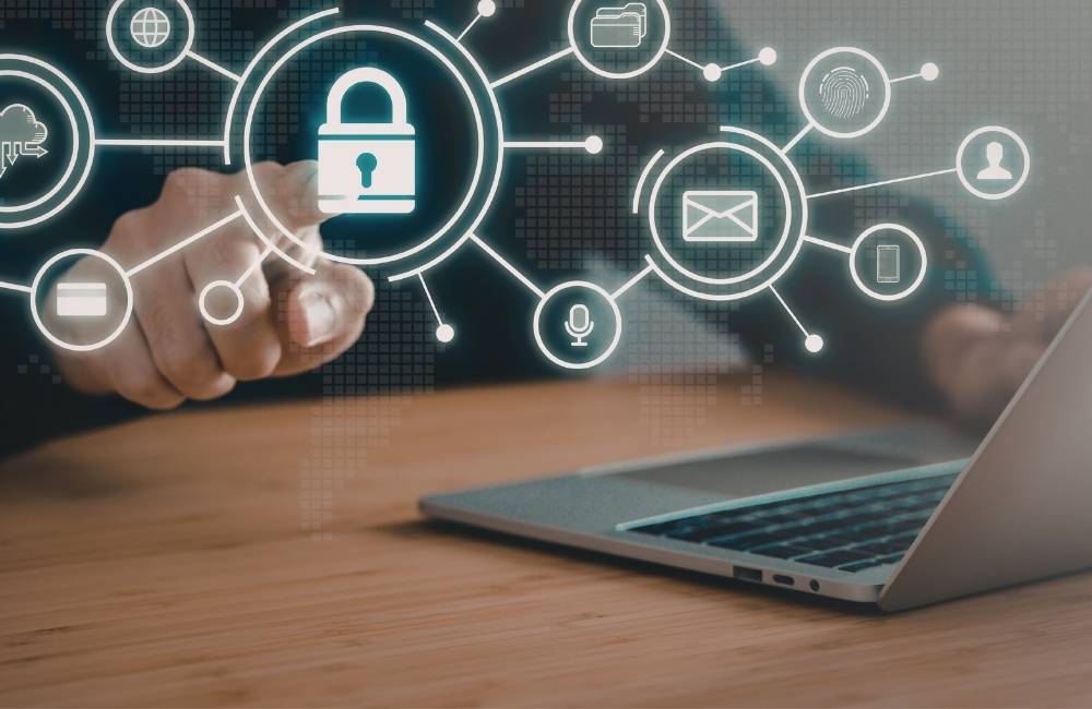 ノートパソコンの画面上に、南京錠やクラウド、Wi-Fiなどのセキュリティ関連アイコンが青白く浮かび上がっているイメージ図。