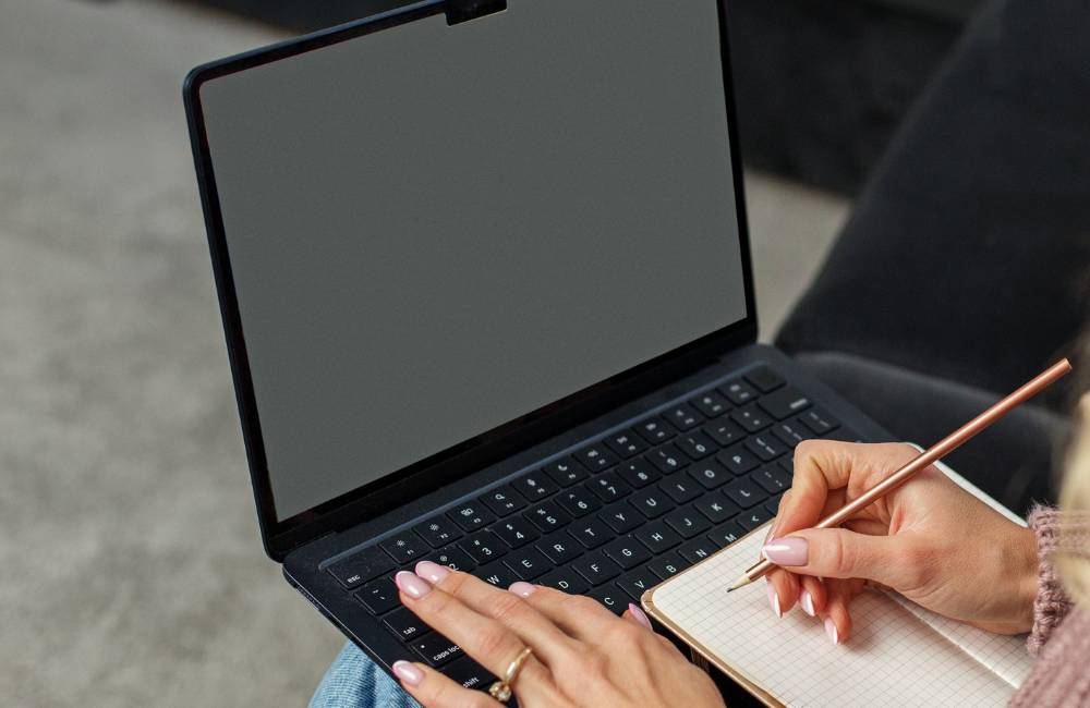 ノートパソコンを開きながら手書きのメモ帳にペンで書き込みをする、前向きな作業風景