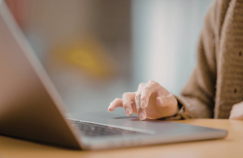 カフェのような場所でリラックスしてノートパソコンのタッチパッドを操作する人の指先のアップ