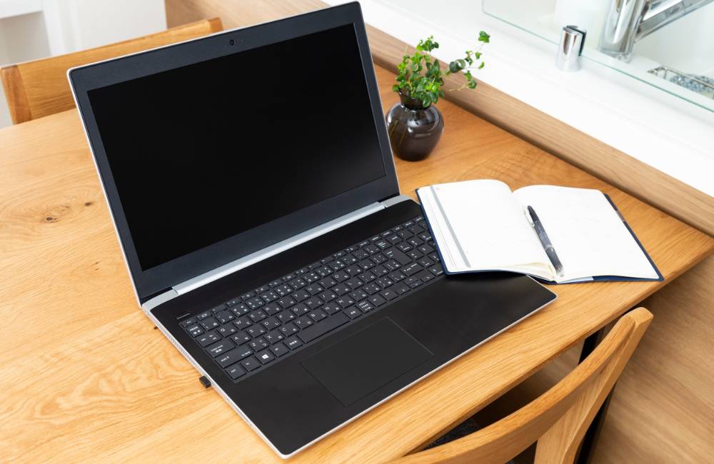 自宅の木製テーブルに置かれたノートパソコンとノート、ペン。テレワークや学習での利用シーン