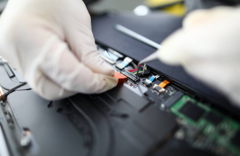 手袋を着用した専門スタッフが、ピンセットを使用してパソコン内部の精密なパーツを丁寧にメンテナンスしている様子