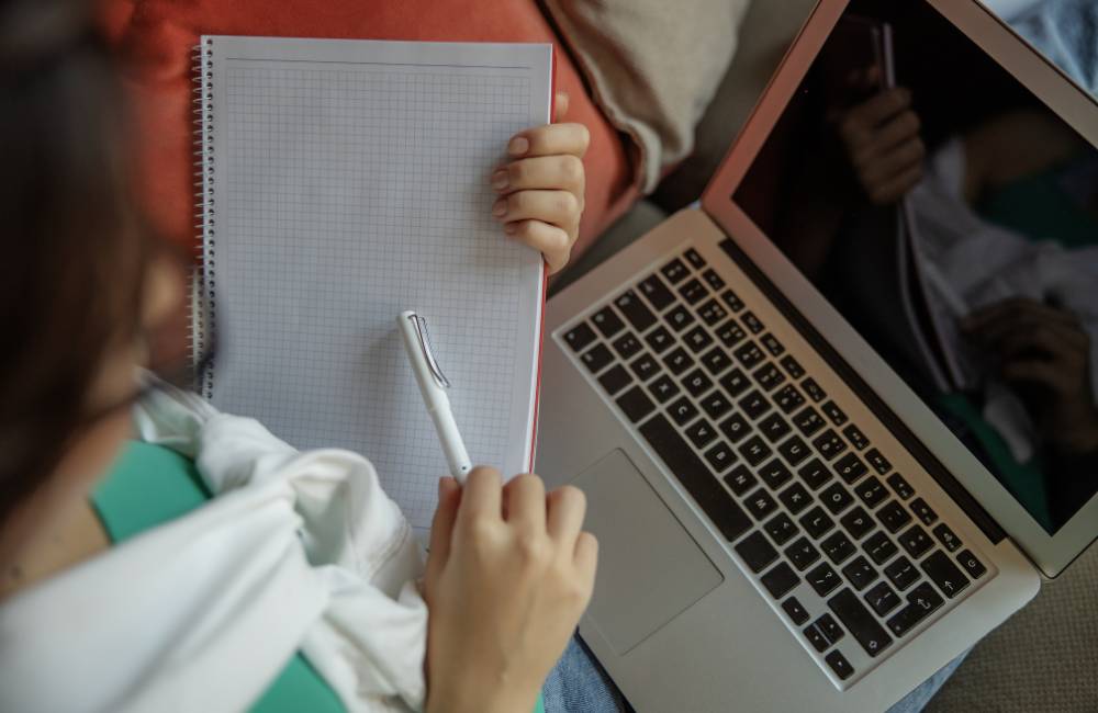 ノートパソコンの横で、白紙のノートとペンを持ち、これから学んだことを整理しようとしている人の上からのアングル